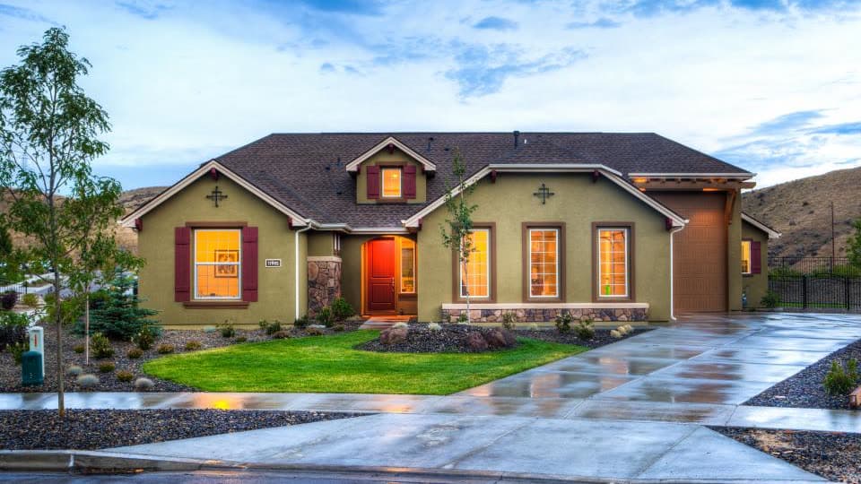 Single-story stucco house with a lawn and a wet driveway at dusk